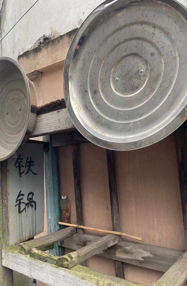 大団古鎮の鉄鍋専門店。軒先に大きな鉄鍋が2つ吊るされ、板壁に铁锅の手書き文字